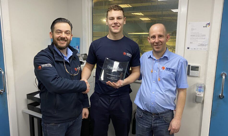 Three employees smiling at camera with award, two are shaking hands