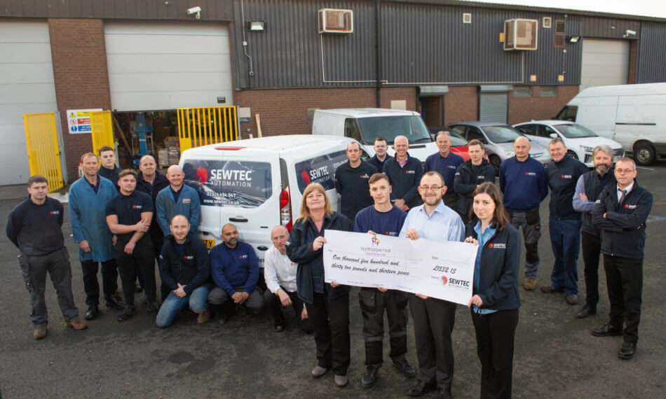 Full team photo outside of warehouse holding cheque