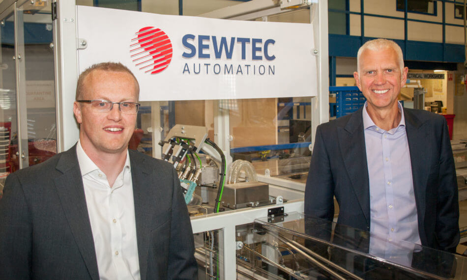 Two males smiling in front of a Sewtec Automation logo