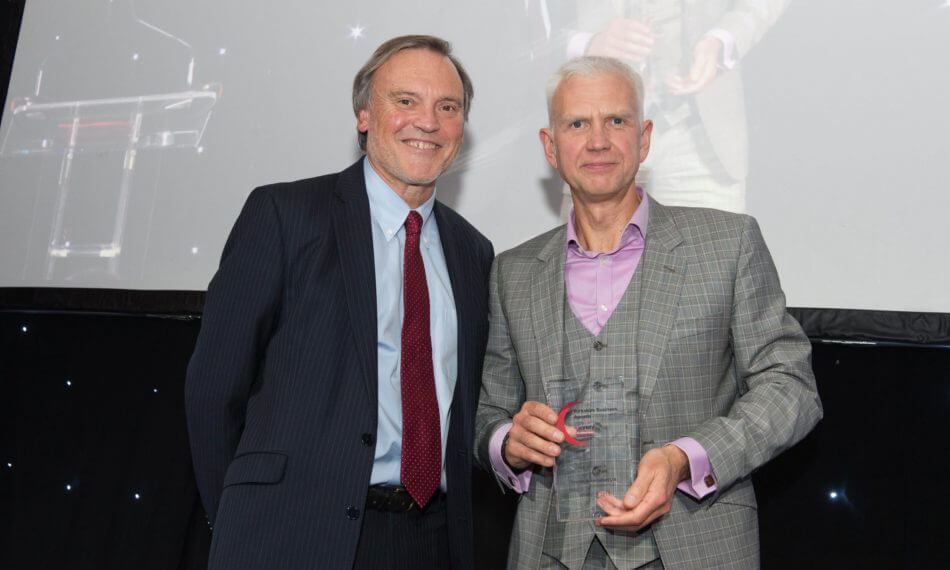 Two males smiling at camera with an award