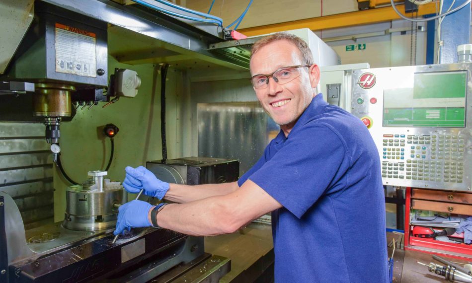 Male employee building machine whilst smiling at camera