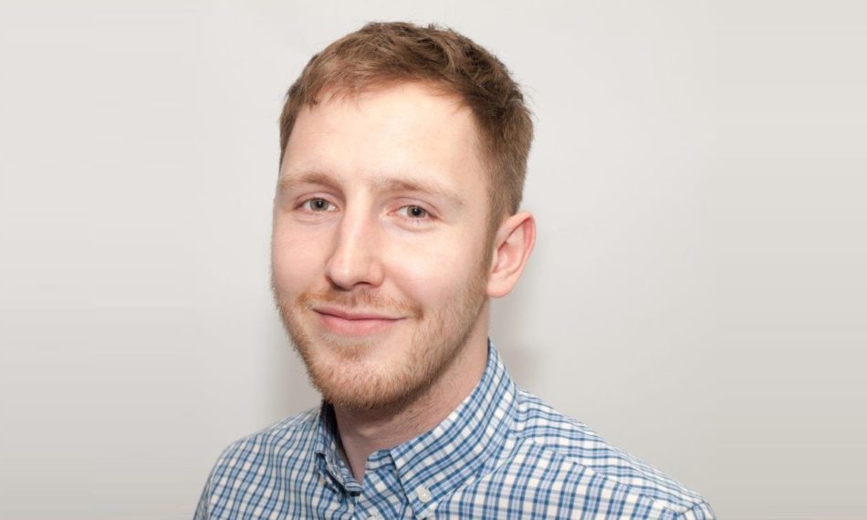 Male employee smiling at camera in front of white wall