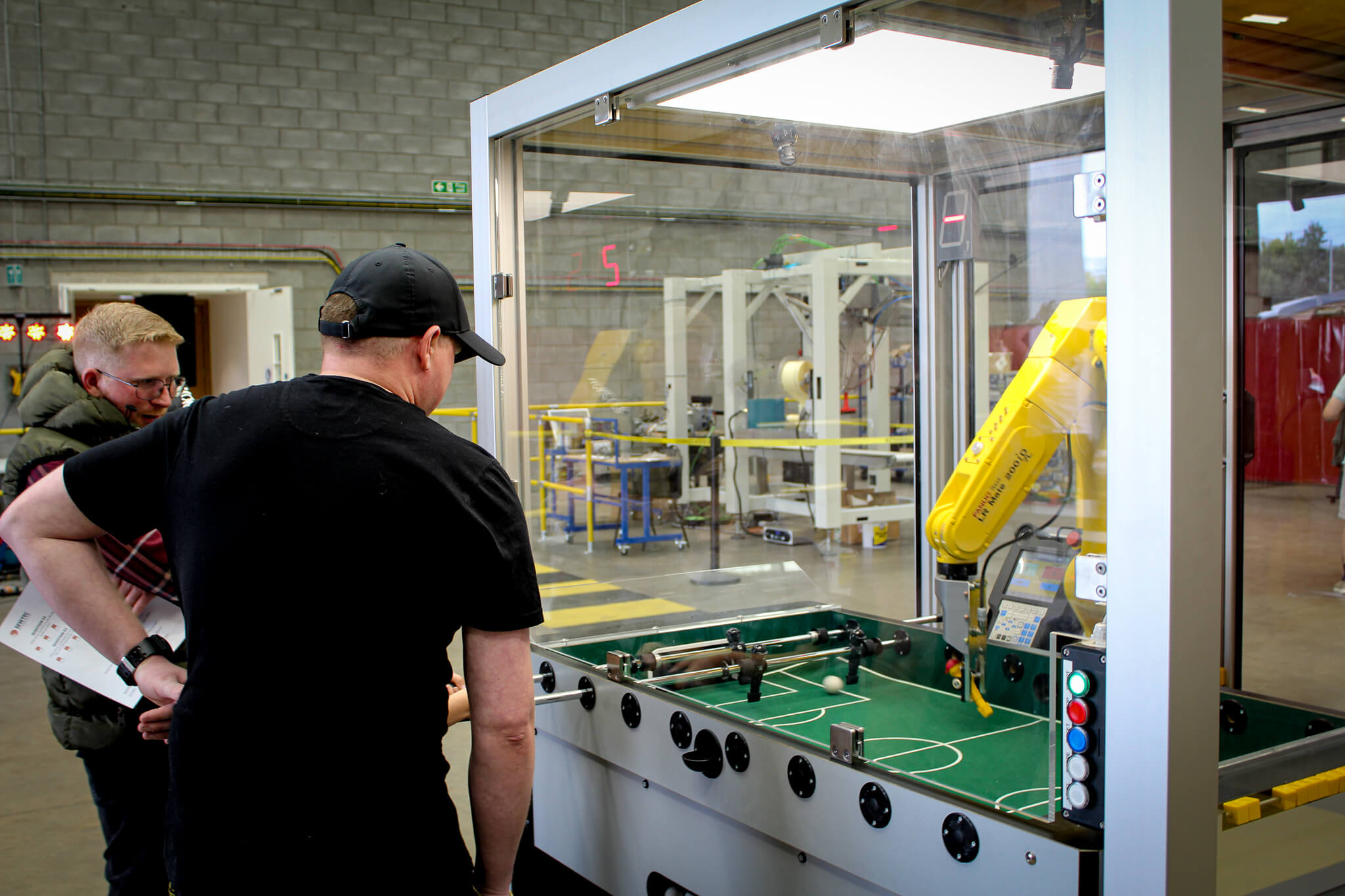 Two team members playing against a robot at table football